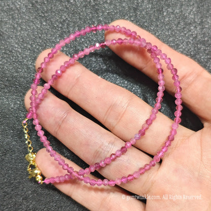 Coiled 3mm faceted pink tourmaline gemstone necklace held across fingers for layered jewelry displays
