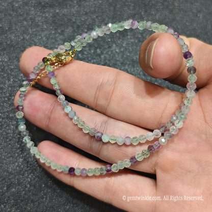 Coiled 3mm faceted rainbow fluorite gemstone necklace held across fingers for layered necklace styling