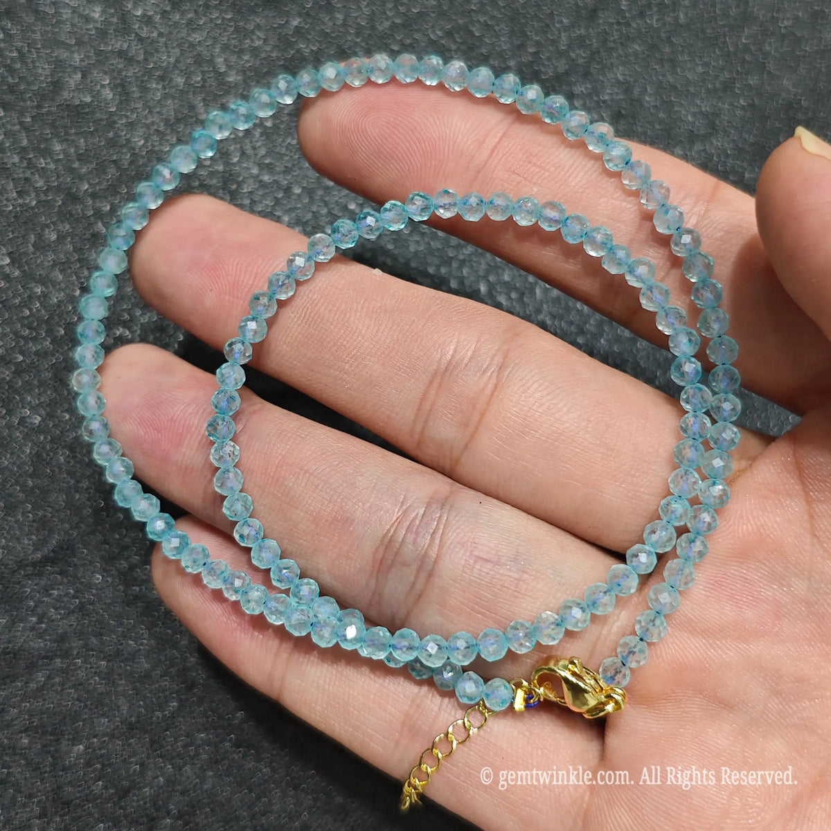 Coiled 3mm faceted sky blue topaz gemstone necklace held across fingers for layered jewelry styling