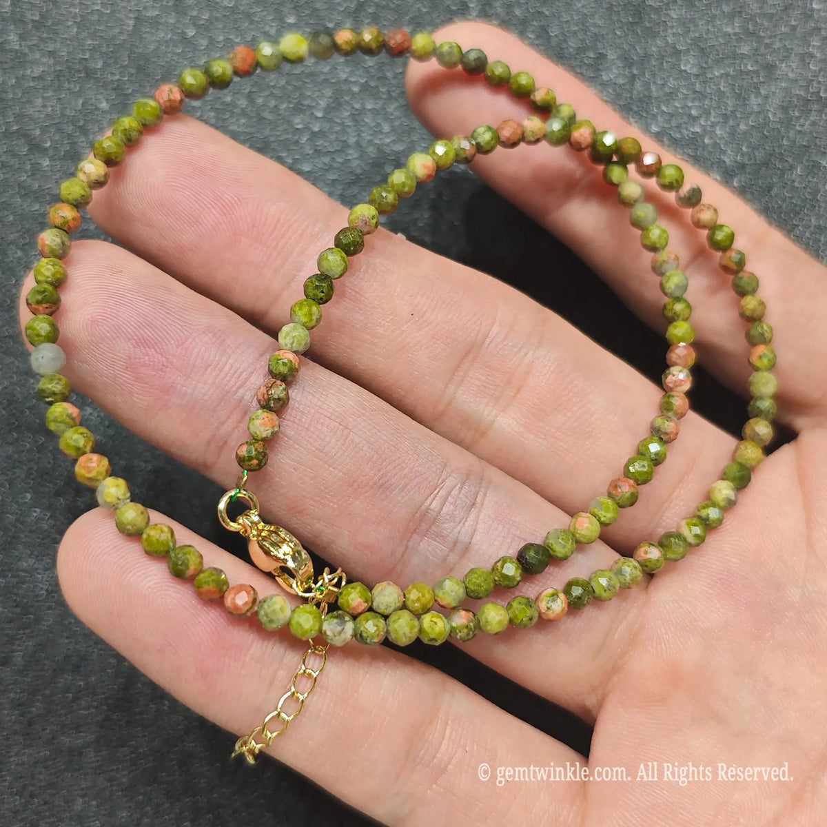 Coiled 3mm faceted unakite gemstone necklace held across fingers for layered jewelry displays