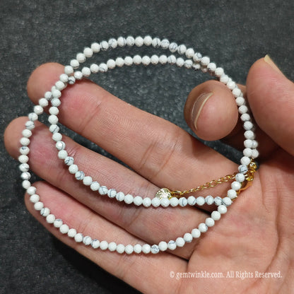 Coiled 3mm faceted white howlite gemstone necklace held across fingers for stackable necklace styling
