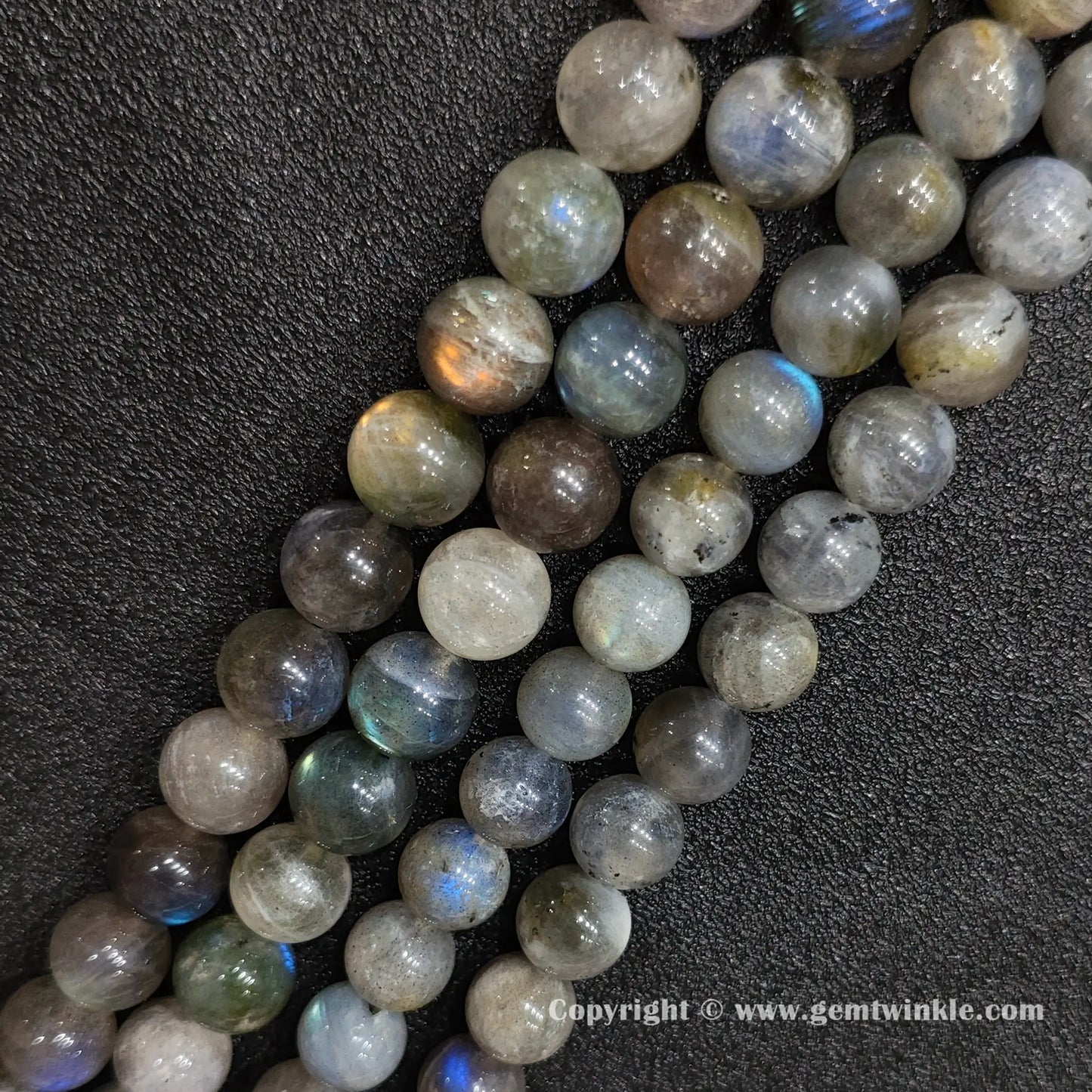 Angled view of chunky dark grey moonstone gemstone strands displaying golden and blue optical light reflections