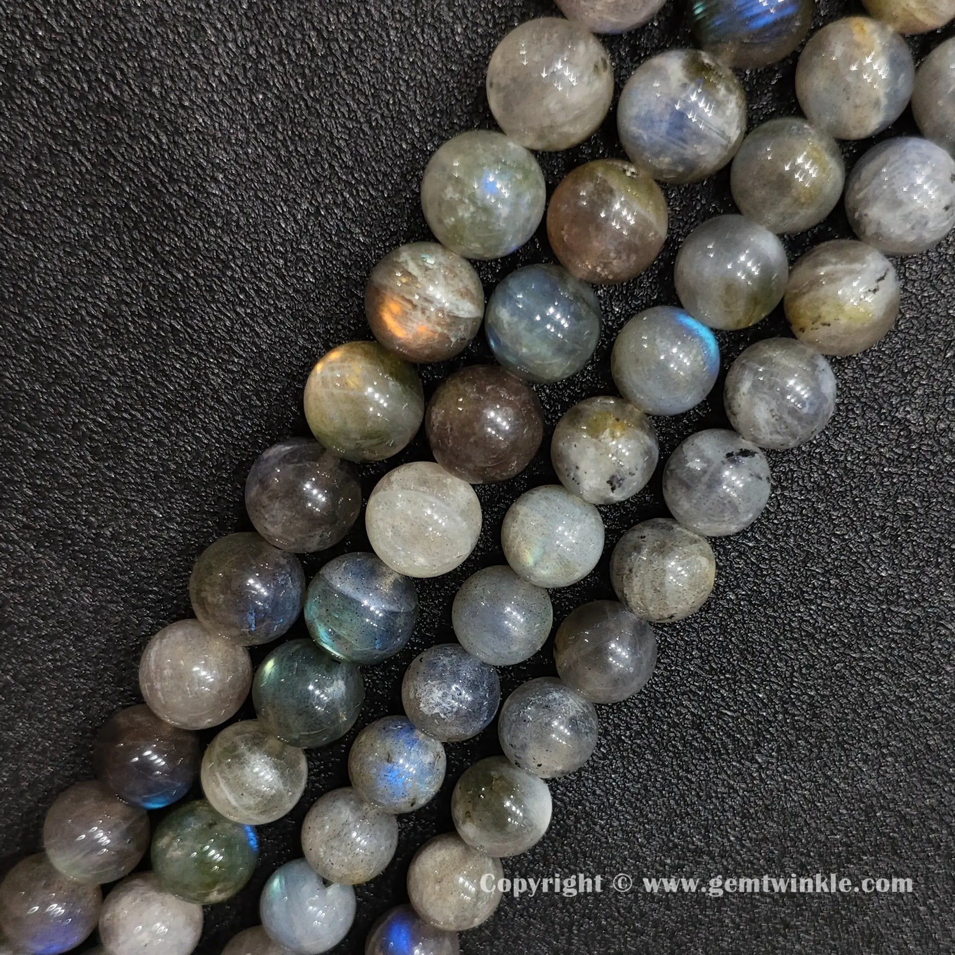 Angled view of chunky dark grey moonstone gemstone strands displaying golden and blue optical light reflections