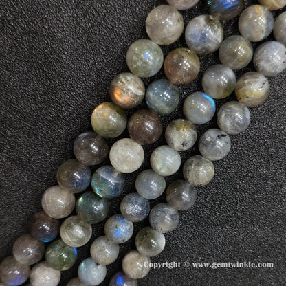 Angled view of chunky dark grey moonstone gemstone strands displaying golden and blue optical light reflections