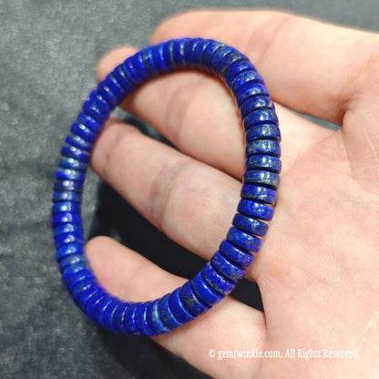 Full view of a deep blue lapis lazuli heishi bead stretch bracelet resting on hand over textured dark background