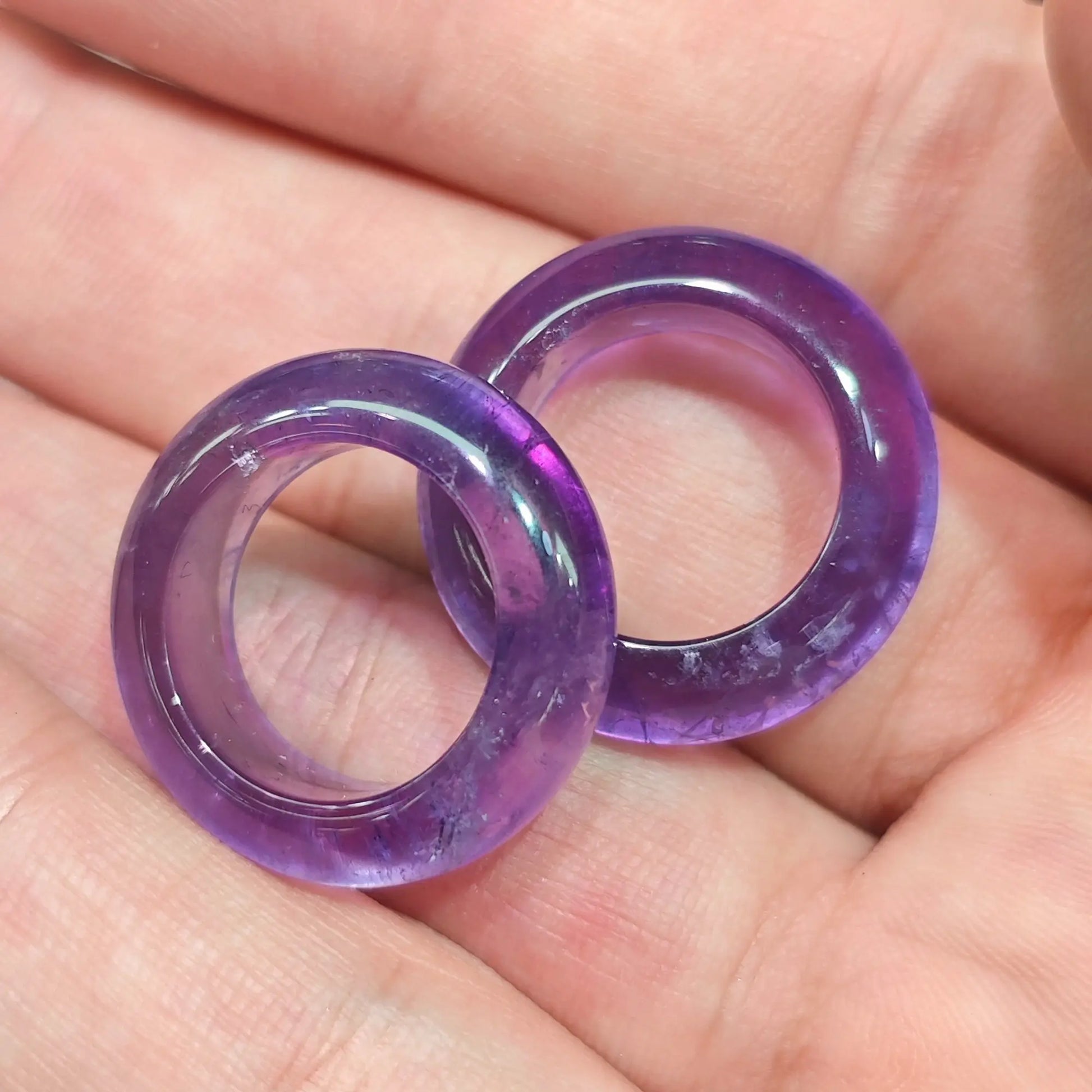 Hand holding two deep purple amethyst solid crystal ring bands 14-18mm showing rich violet color and smooth polished finish