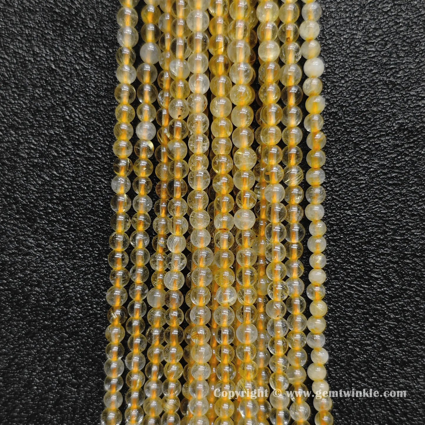 Detailed shot of real 3mm small crystal beads with semi transparent quartz bodies and fine golden hair inclusions for layering jewelry designs