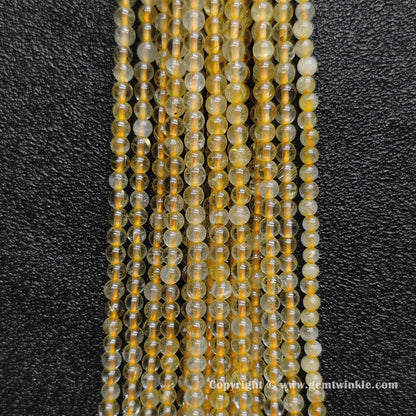 Detailed shot of real 3mm small crystal beads with semi transparent quartz bodies and fine golden hair inclusions for layering jewelry designs