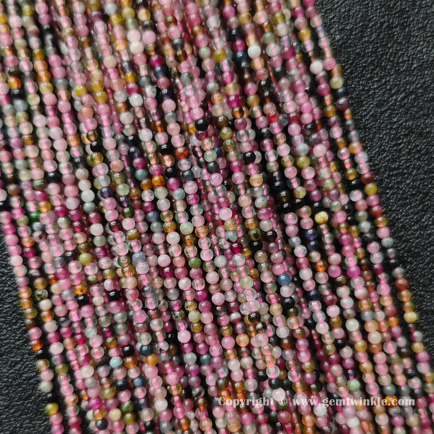 Close up detail of delicate semi translucent multi color tourmaline 2mm micro round beads