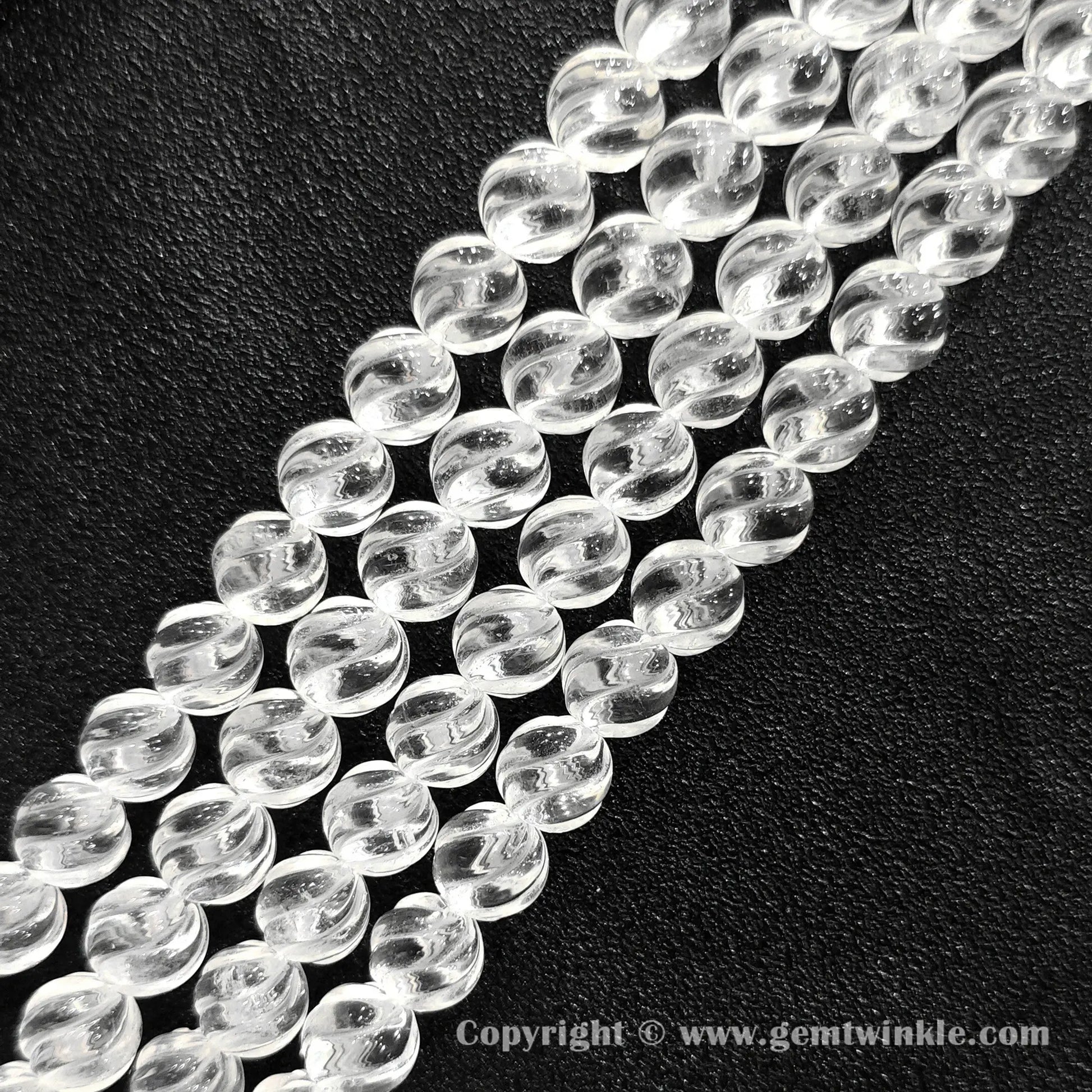 Close up view of diagonal swirl carved clear quartz beads showing light reflections