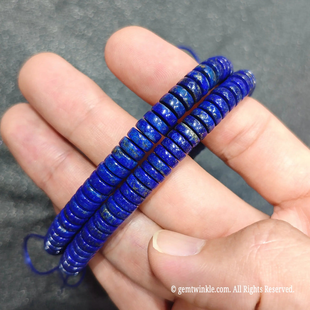 Hand holding stacked natural lapis lazuli abacus bead stretch bracelets showcasing dynamic blue tones