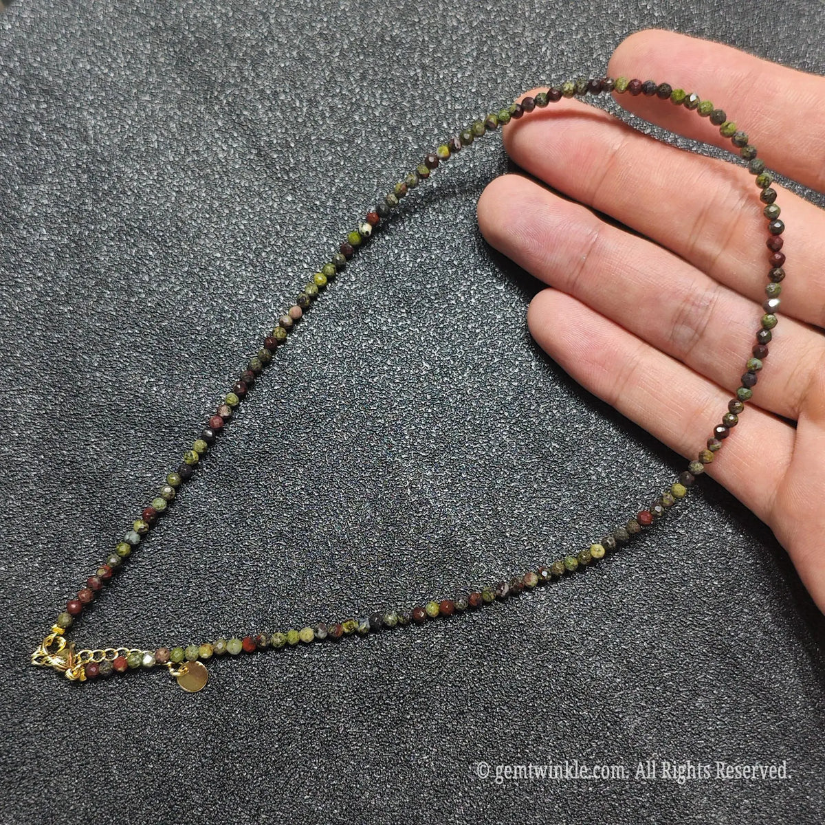 Hand holding 3mm micro faceted Dragon Blood Jasper necklace strand showing dark green and red mineral speckled matrix