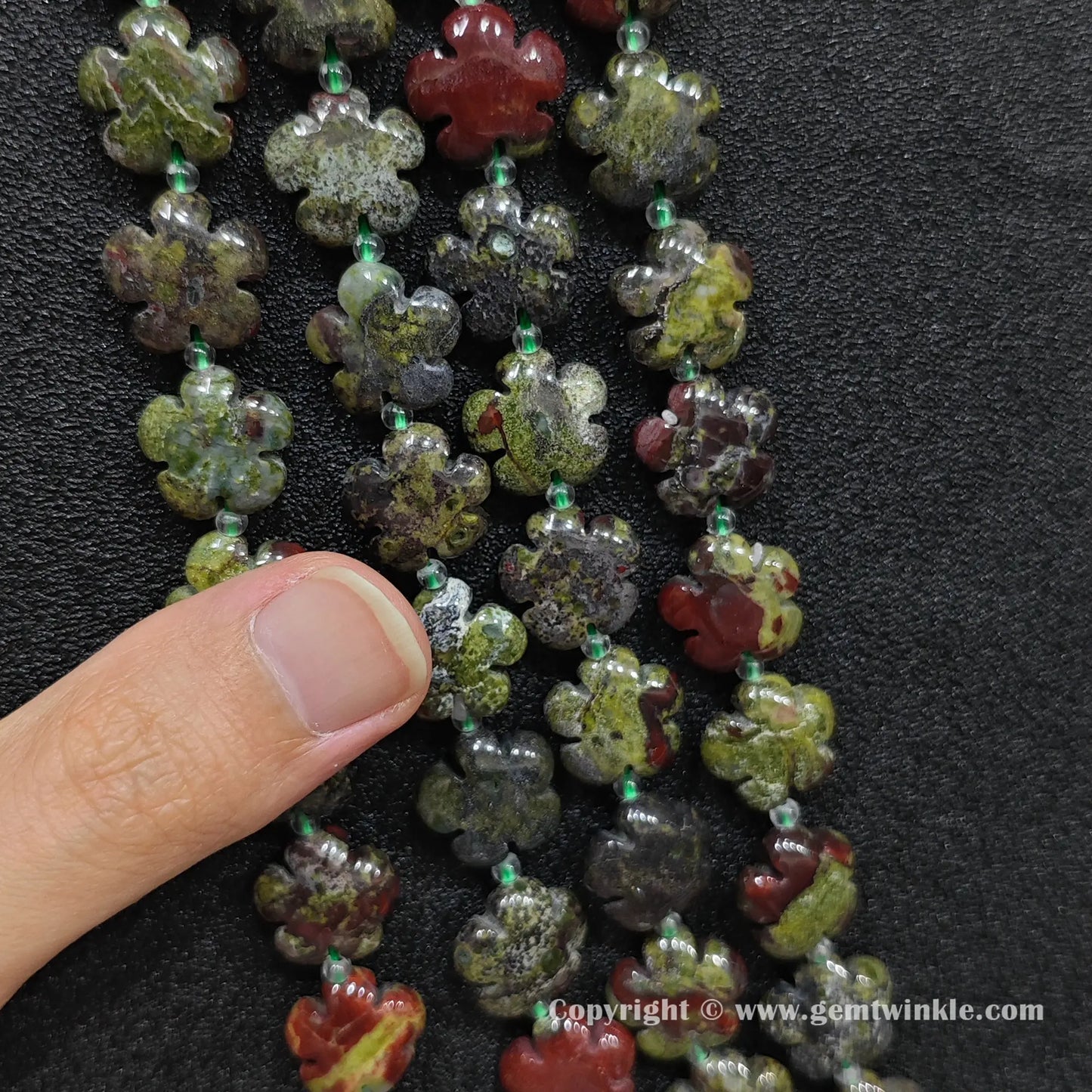 Close up view of dragon blood stone plum blossom carved beads held on fingers for quality preview