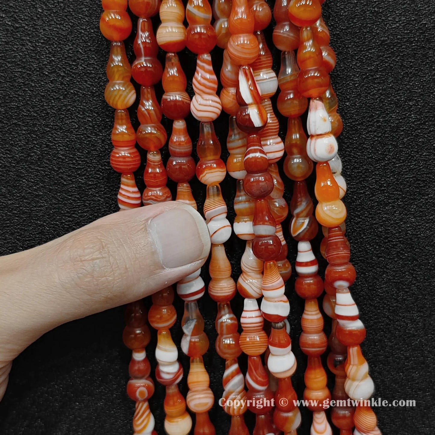 Close up view of color-dyed banded agate calabash beads held on fingers for quality preview