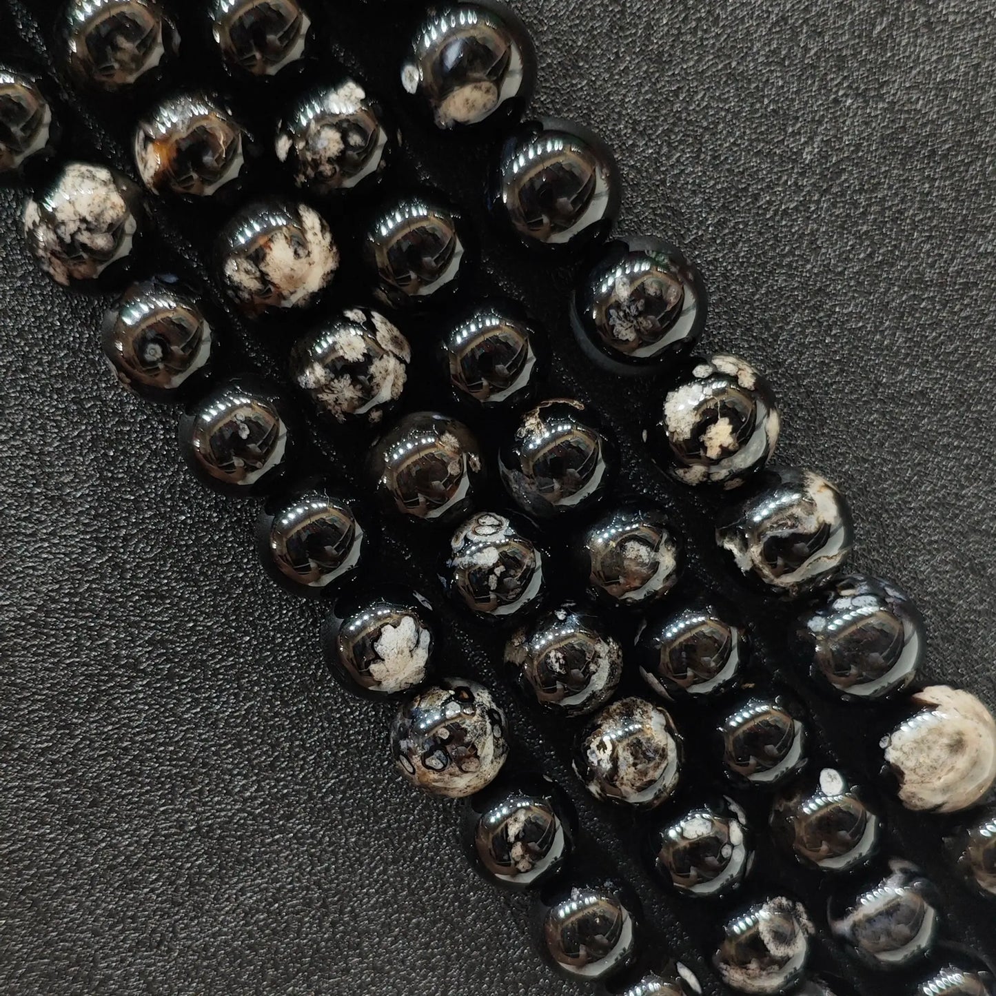 Close up view of dyed black cherry blossom agate crystal beads strands showing high contrast white floral plumes over a natural agate base in image_be1c2a.jpg
