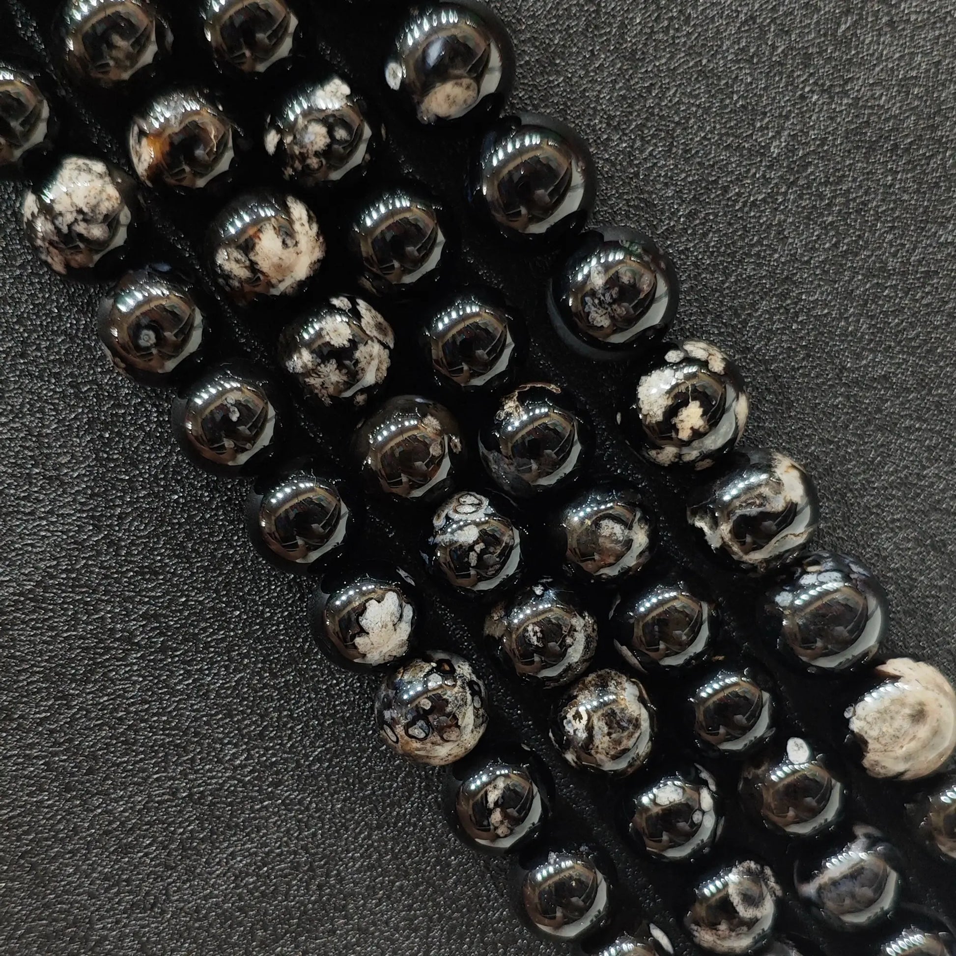 Close up view of dyed black cherry blossom agate crystal beads strands showing high contrast white floral plumes over a natural agate base in image_be1c2a.jpg