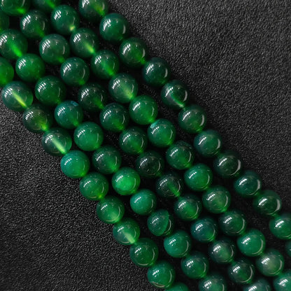 Vibrant dyed green agate smooth round beads bulk strands showing rich glossy surface on dark backdrop
