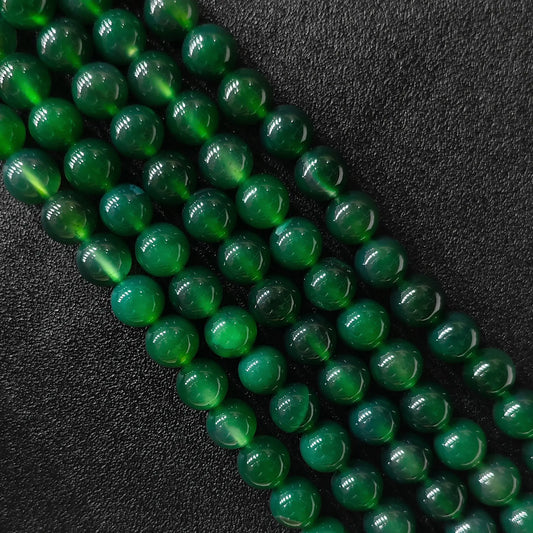 Vibrant dyed green agate smooth round beads bulk strands showing rich glossy surface on dark backdrop