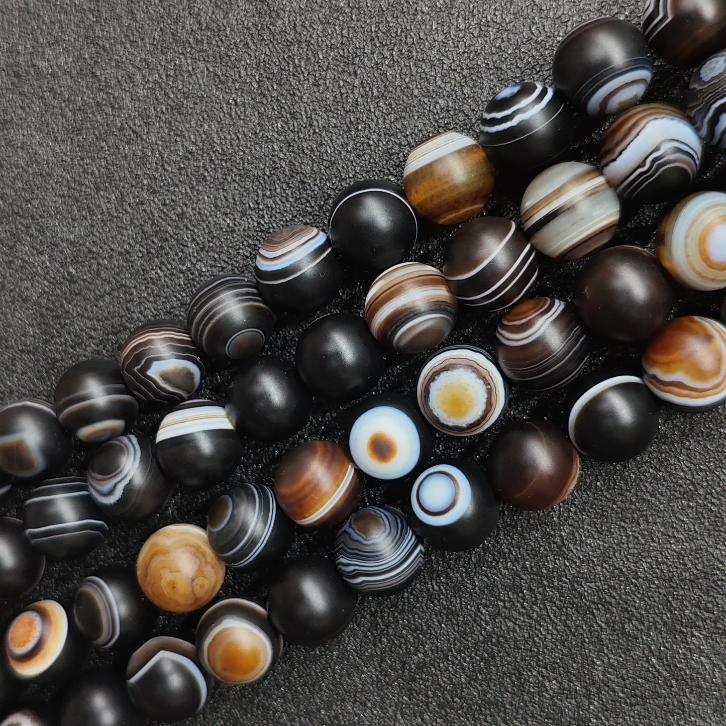 dyed matte eye agate beads for jewelry making showing frosted black and white banded strands from 6mm to 14mm on a dark surface in image_76a81c.jpg