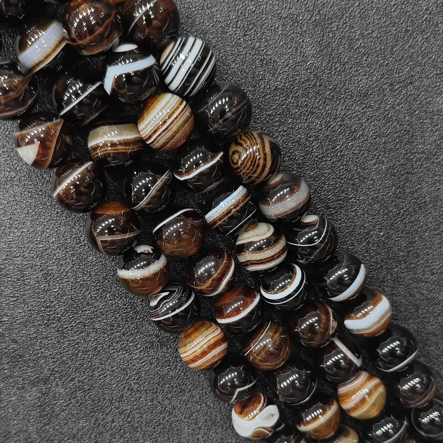 dyed natural gemstone beads for jewelry making showing high contrast grey and brown banded agate strands from 6mm to 14mm on a black surface