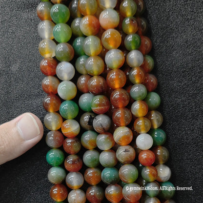 Hand holding Peacock Agate dyed stone beads to show size and color quality
