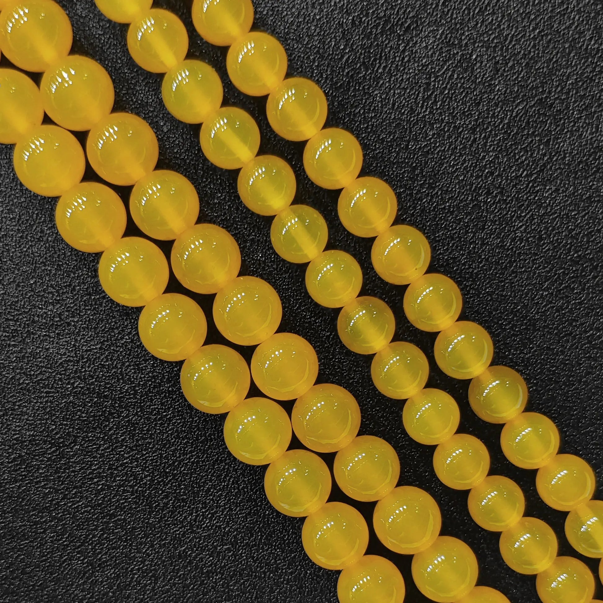 Three close up bulk strands of dyed vibrant yellow agate smooth round beads on dark background in image_bca51d.jpg