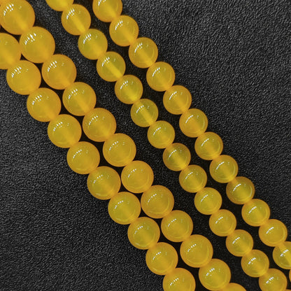 Three close up bulk strands of dyed vibrant yellow agate smooth round beads on dark background in image_bca51d.jpg