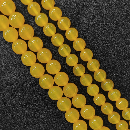Three close up bulk strands of dyed vibrant yellow agate smooth round beads on dark background in image_bca51d.jpg
