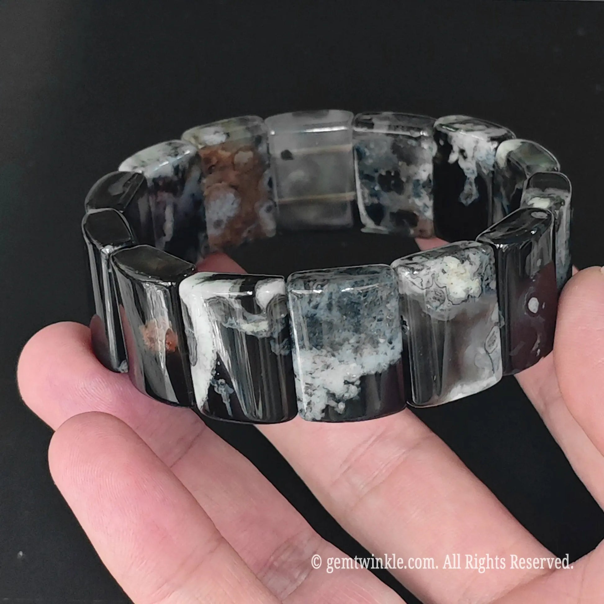Angle view of dyed black cherry blossom agate rectangular plate bead bracelet held in hand highlighting chalcedony plumes