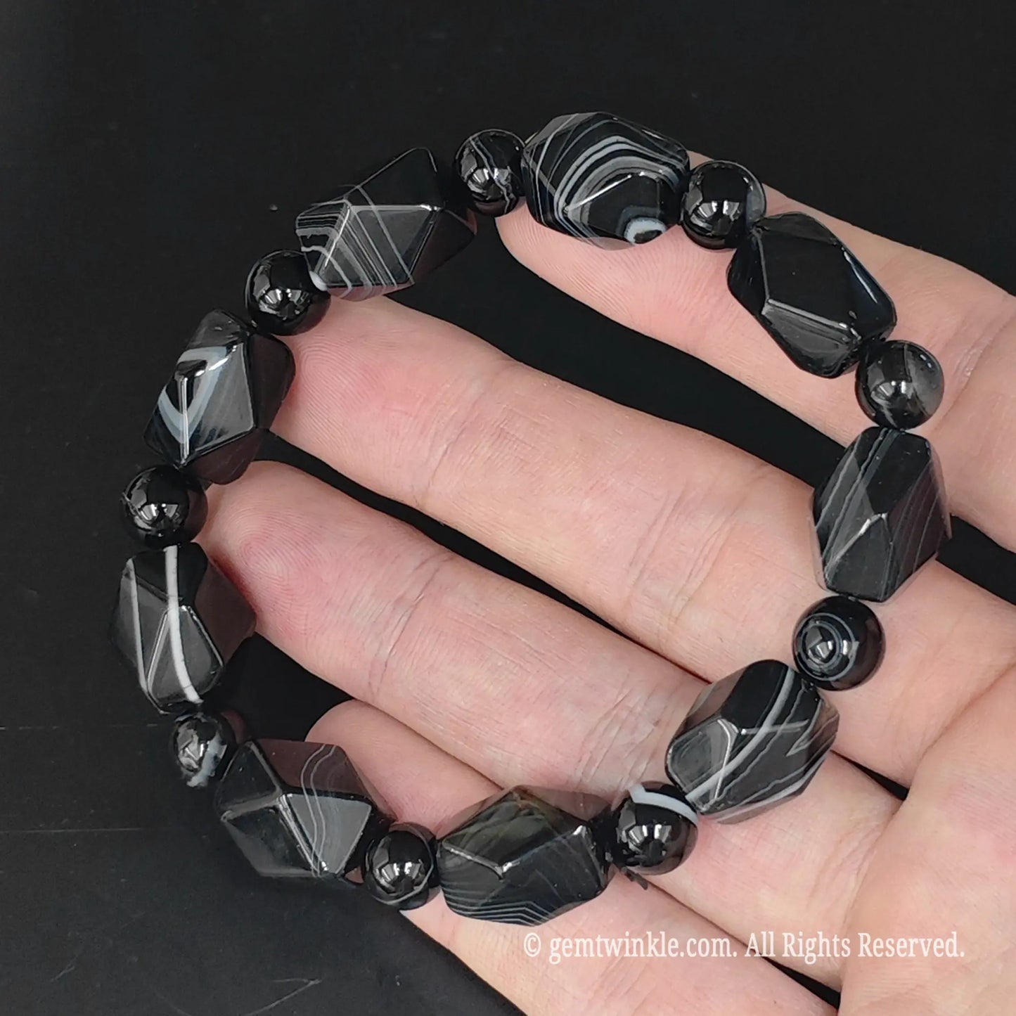 Dyed black silk agate faceted nugget bracelet resting on palm showcasing glossy polish and round spacer beads