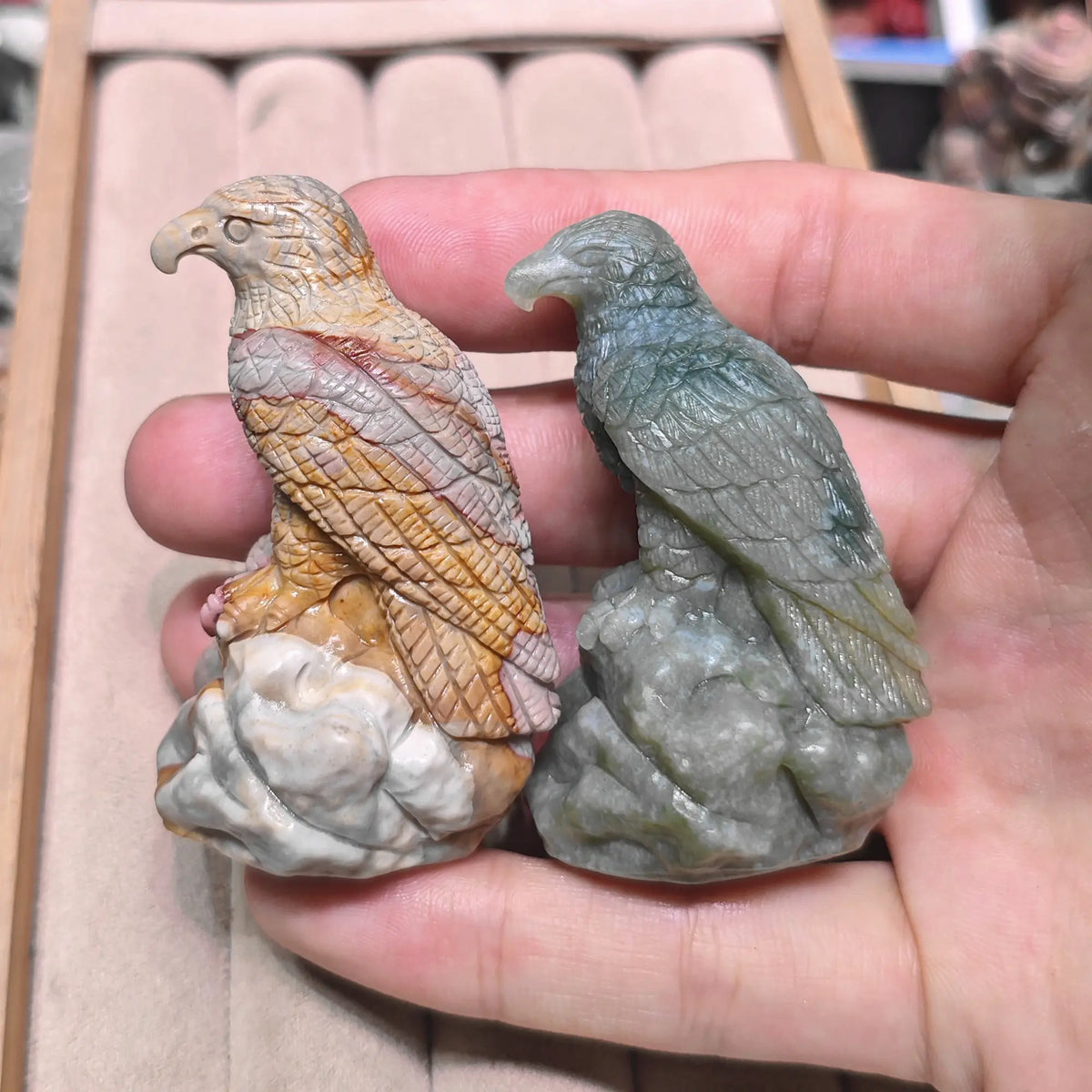 Open hand displaying two perched eagle statues side by side comparing warm amber red and cool sage green color tones