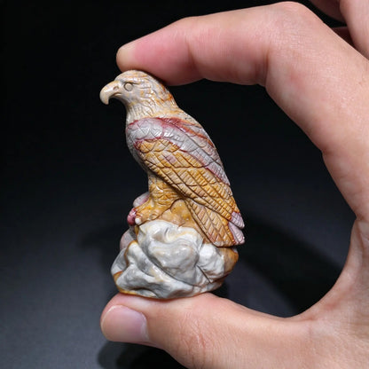 Profile view of a carved eagle statue with golden yellow and rusty red feather detailing held between fingers under studio light