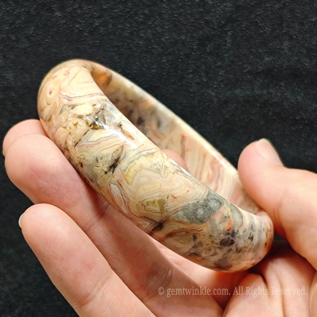 fingers holding natural crazy lace agate bangle displaying rich texture