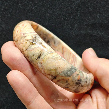 fingers holding natural crazy lace agate bangle displaying rich texture