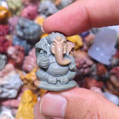 Fingertips holding a slate blue-gray tone miniature Ganesha sculpture with polished smooth finish