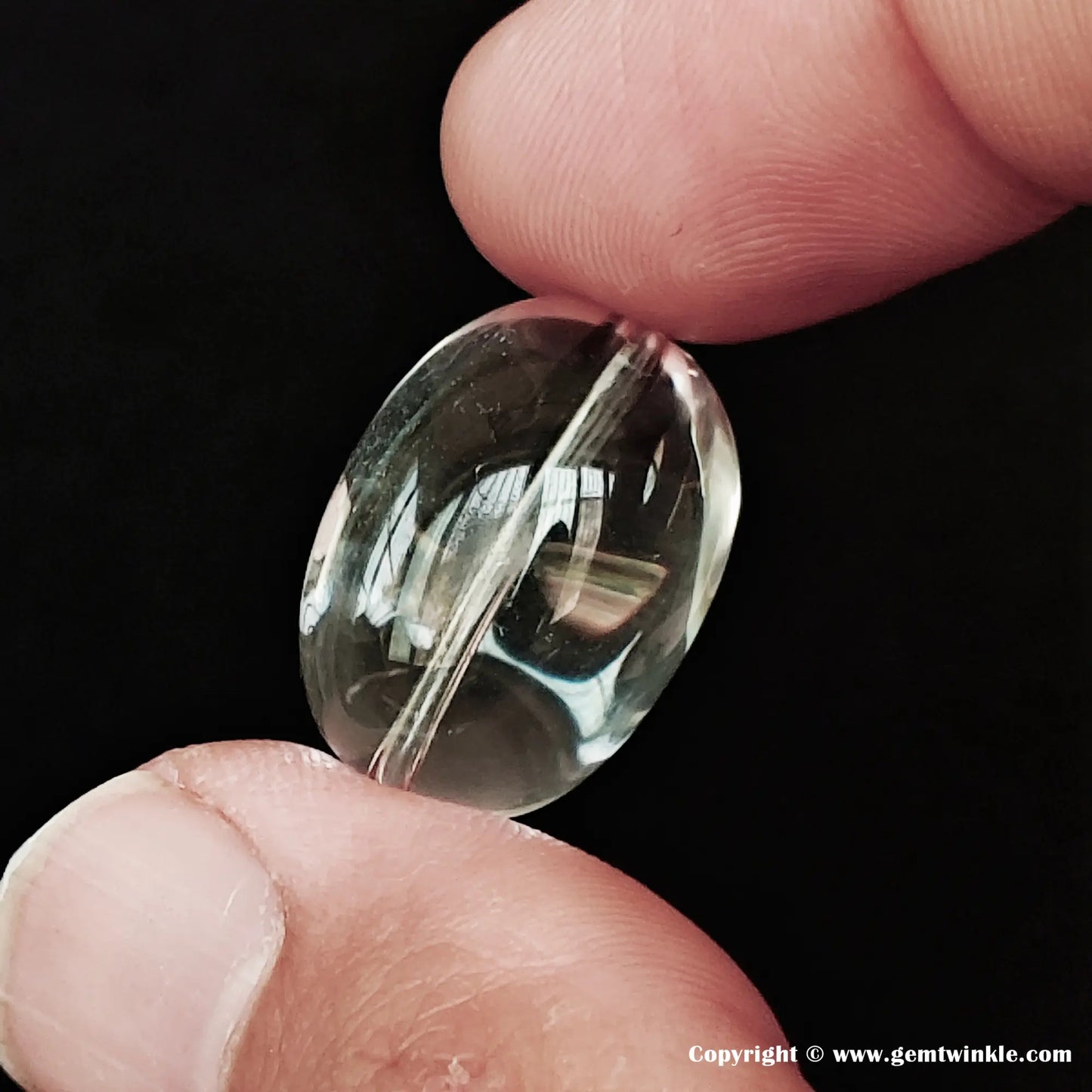 Close-up of a 20-22mm eye-clean natural clear quartz sugar-bean bead held between fingers, showing perfectly clear transparency and pre-drilled hole