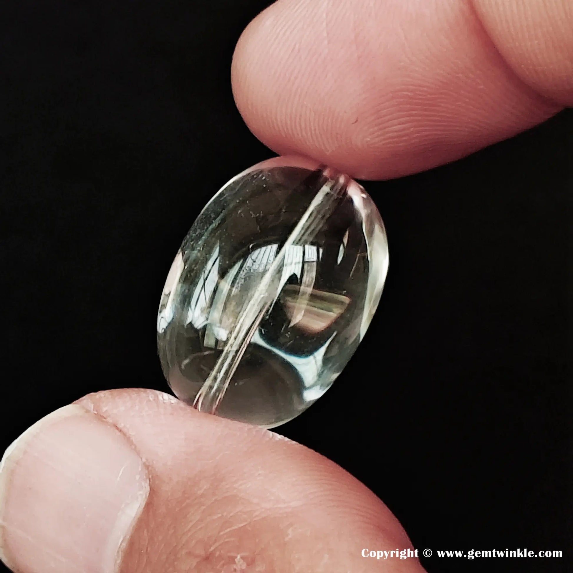 Close-up of a 20-22mm eye-clean natural clear quartz sugar-bean bead held between fingers, showing perfectly clear transparency and pre-drilled hole