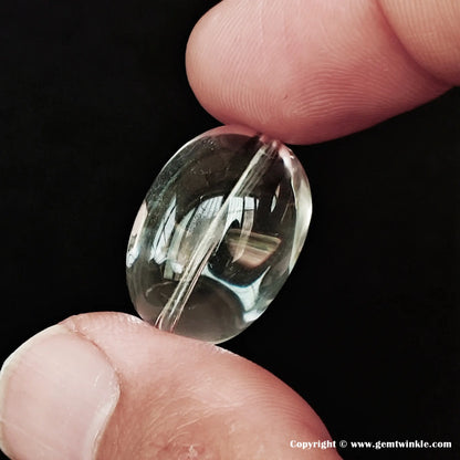 Close-up of a 20-22mm eye-clean natural clear quartz sugar-bean bead held between fingers, showing perfectly clear transparency and pre-drilled hole