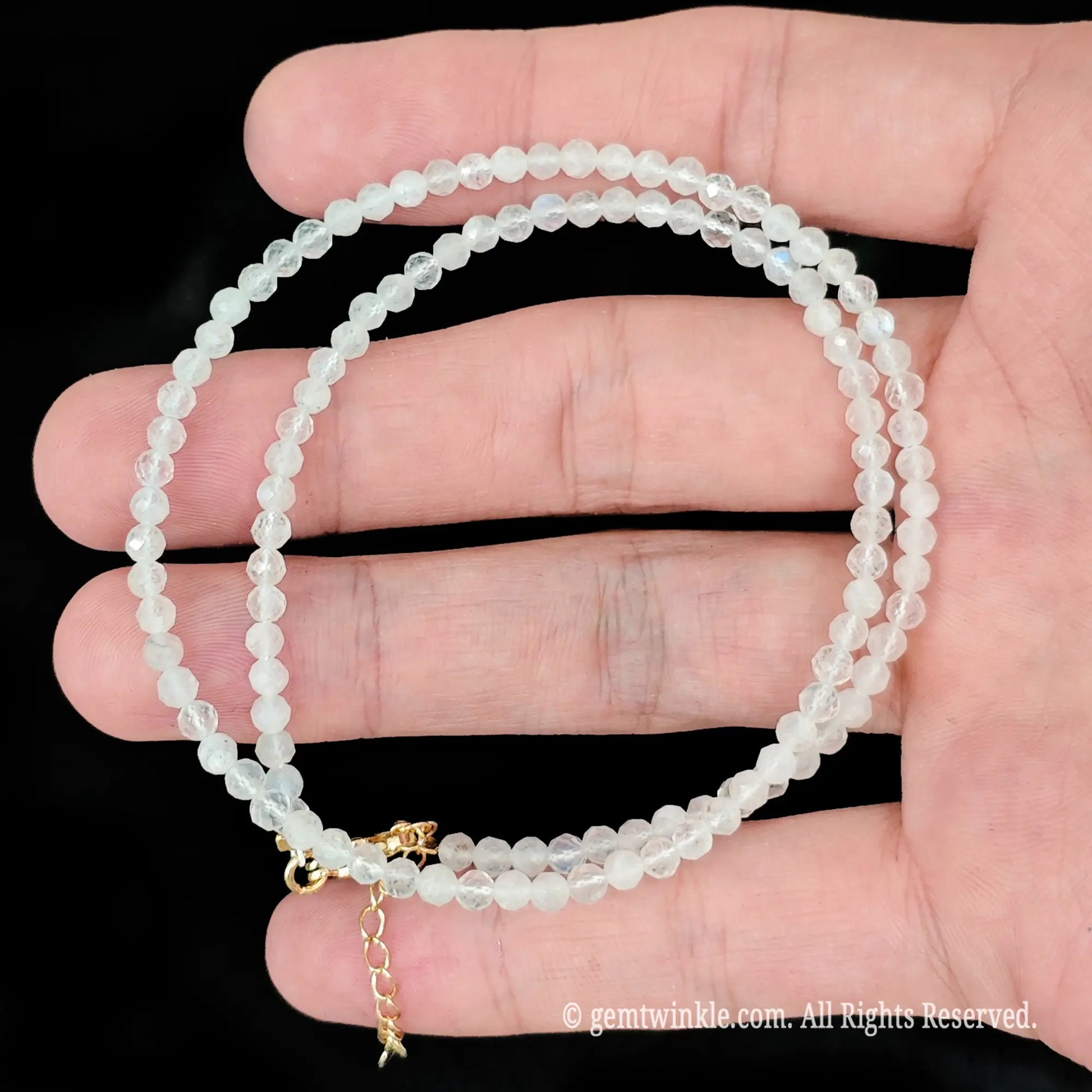 single strand white moonstone beaded necklace coiled across palm showing subtle blue sheen