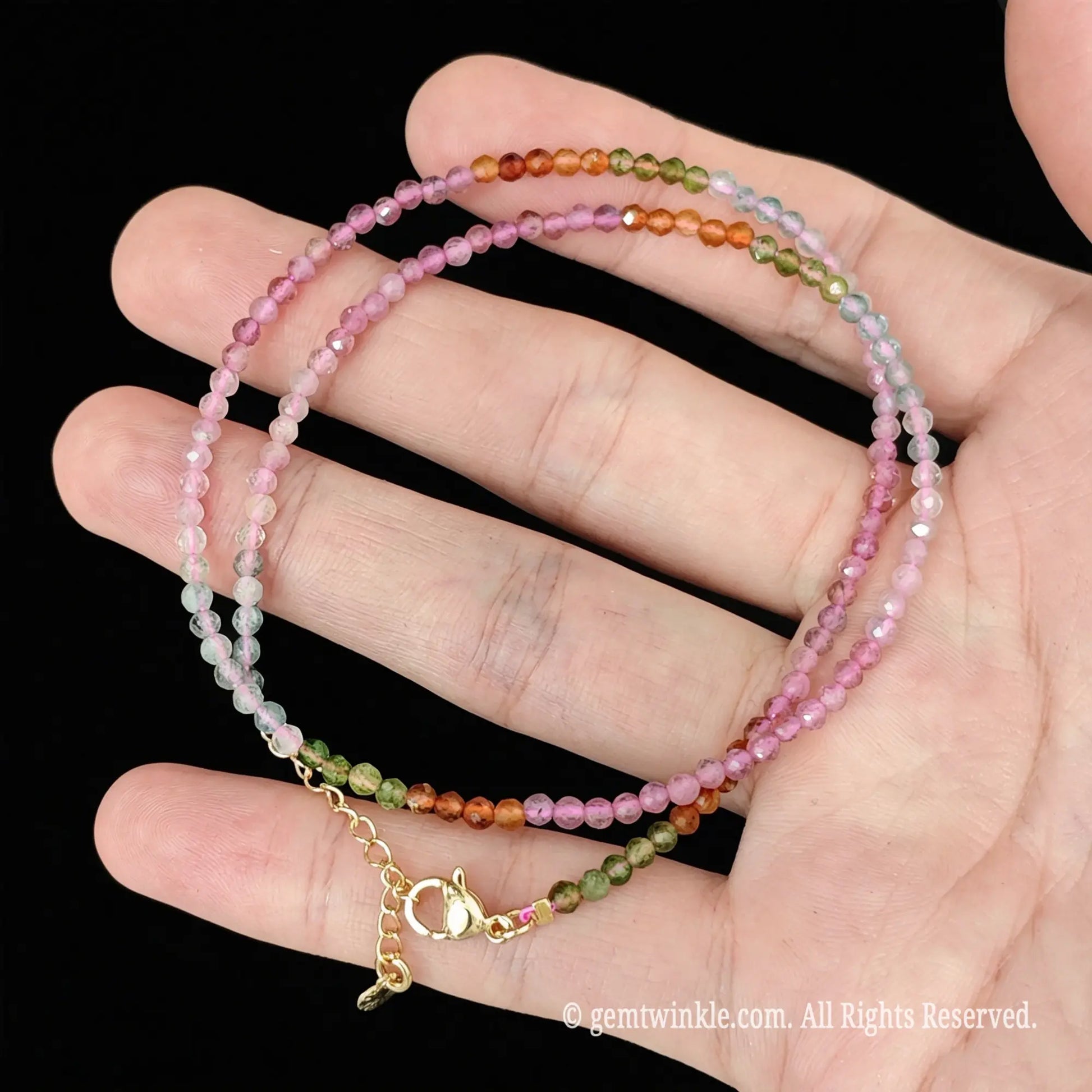 single strand rainbow tourmaline choker necklace coiled across palm showing natural color gradients