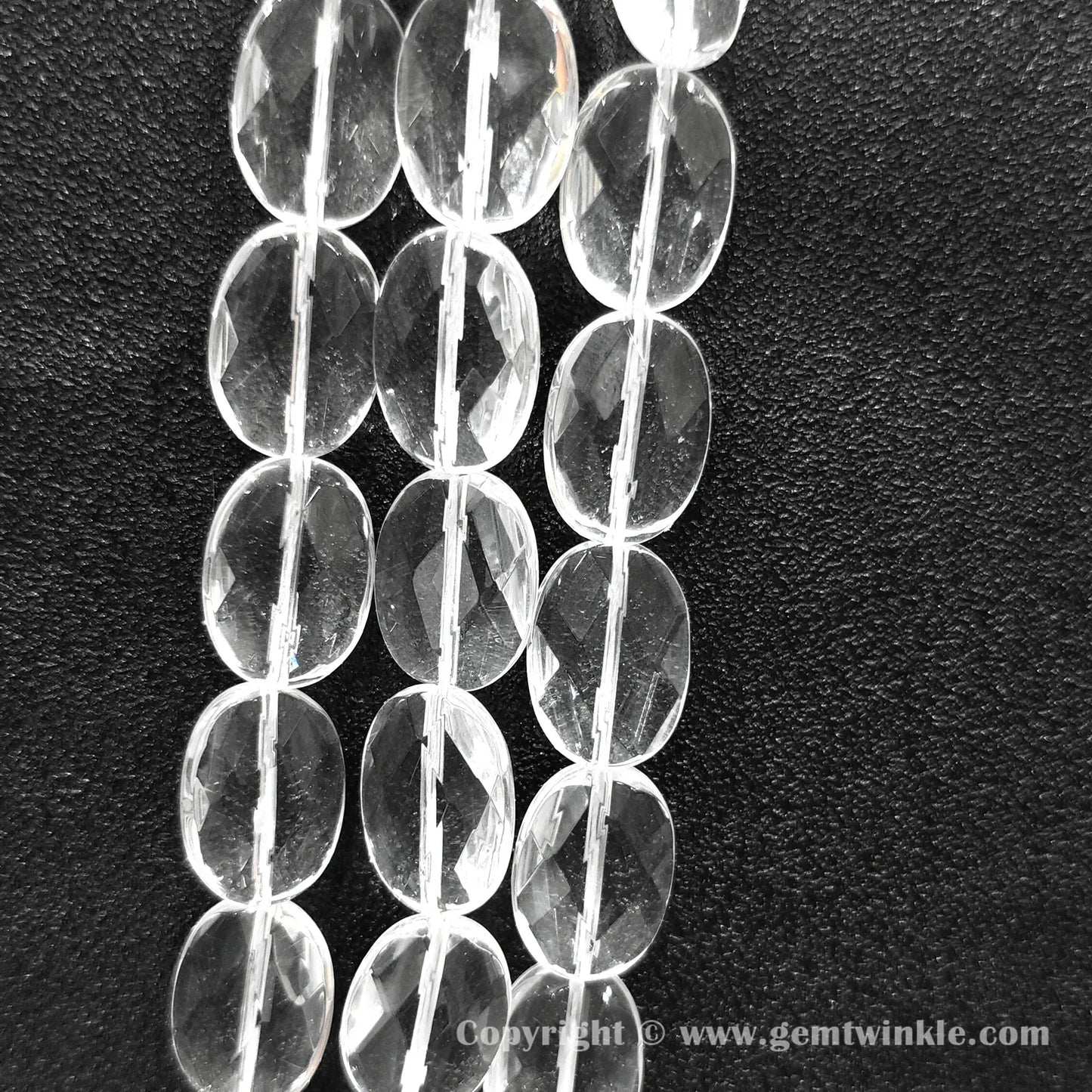 Vertical alignment of faceted oval slice clear quartz beads on dark background
