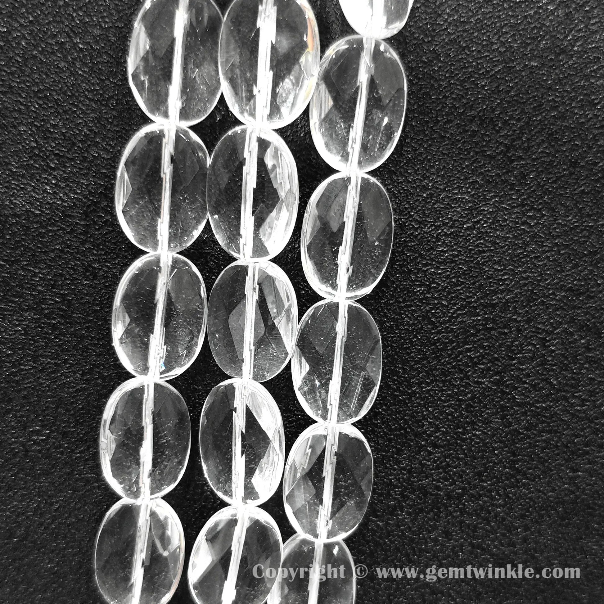 Vertical alignment of faceted oval slice clear quartz beads on dark background