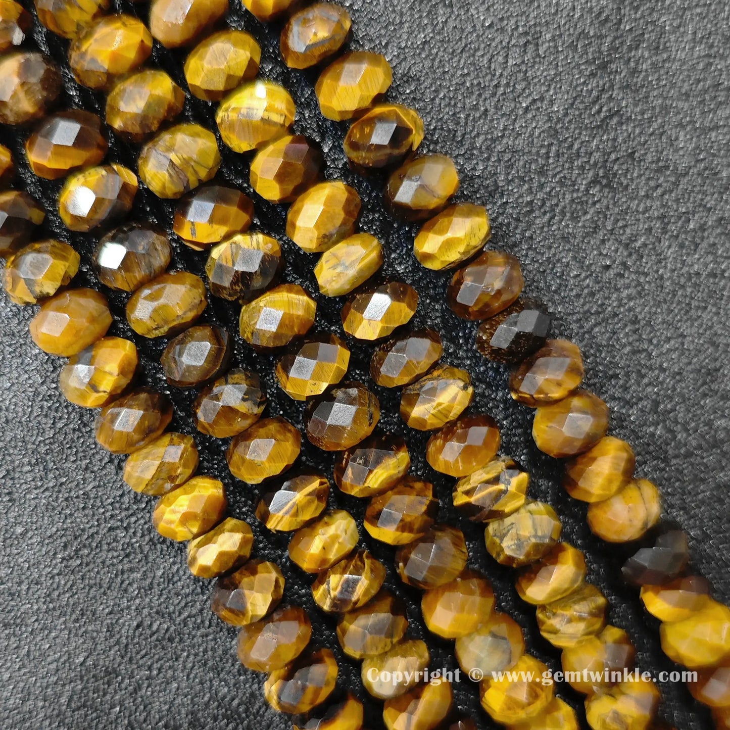 Angled view of 8x5mm and 10x6mm yellow tiger eye faceted disc bead strands laid parallel on dark surface