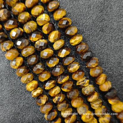 Angled view of 8x5mm and 10x6mm yellow tiger eye faceted disc bead strands laid parallel on dark surface