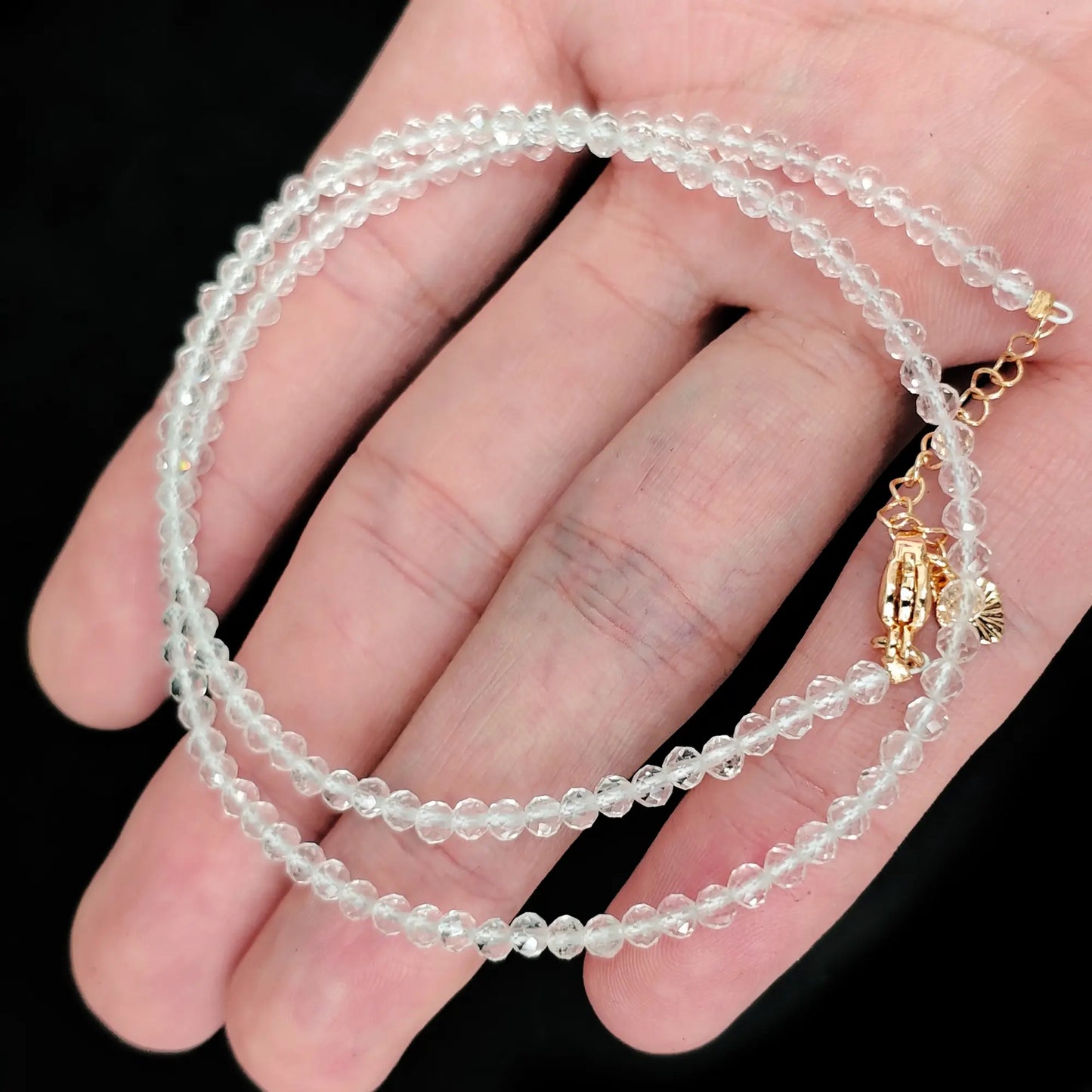 single strand clear quartz beaded necklace coiled across palm showing transparent icy clarity