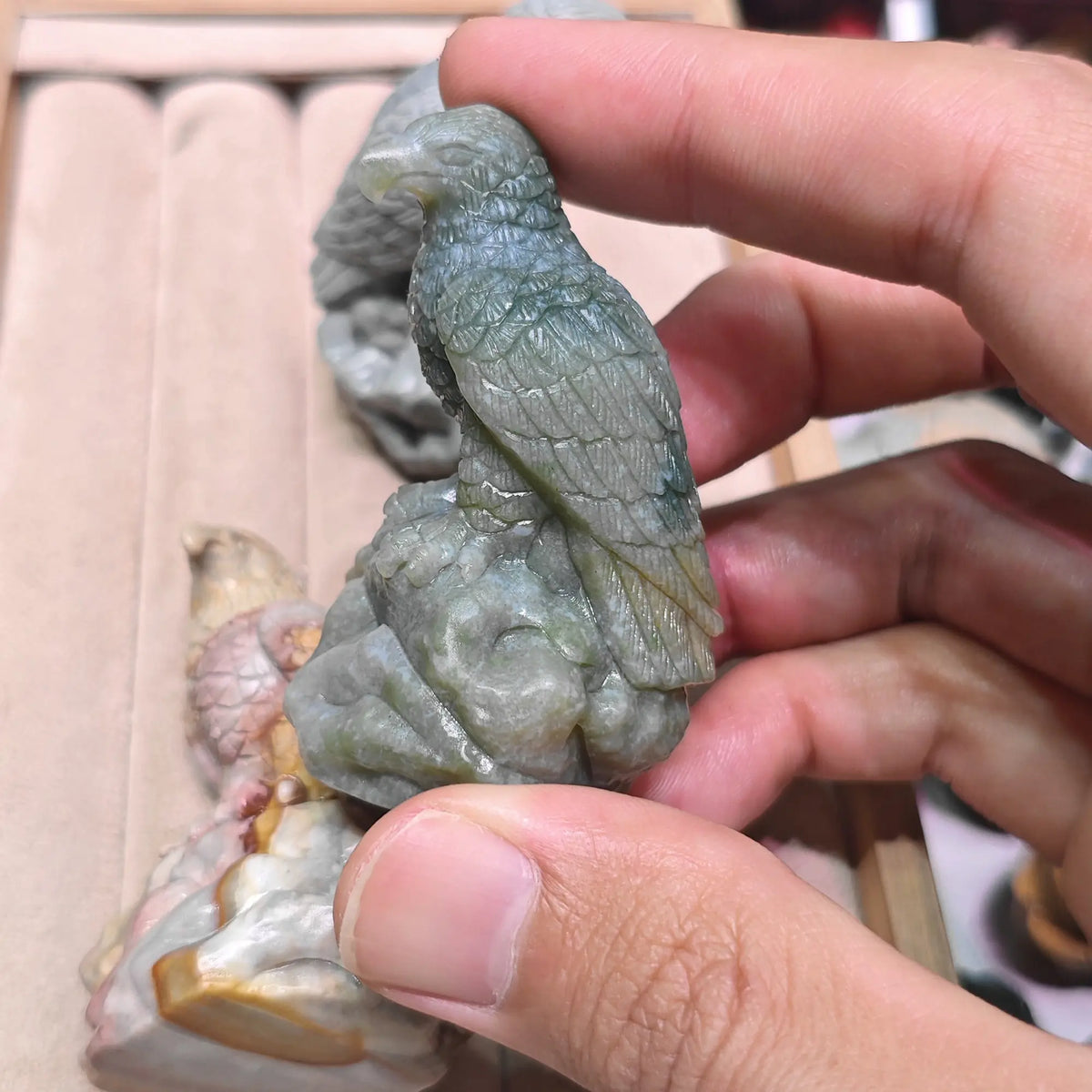 Back view of a sage green falcon figurine held between fingers highlighting feather textures along the spine and tail