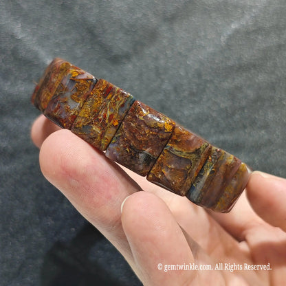 Side view of a fiery pietersite bar cut bangle displaying brecciated silky chatoyant fragments