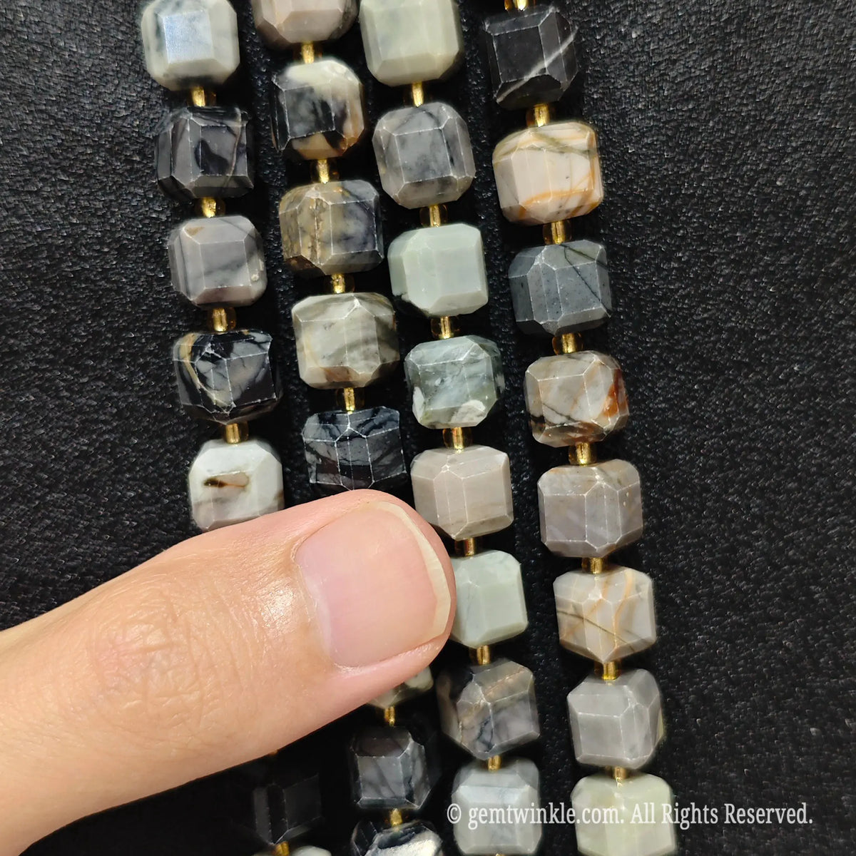 Artisan fingers holding picasso stone strands to demonstrate bead scale and marbleized texture