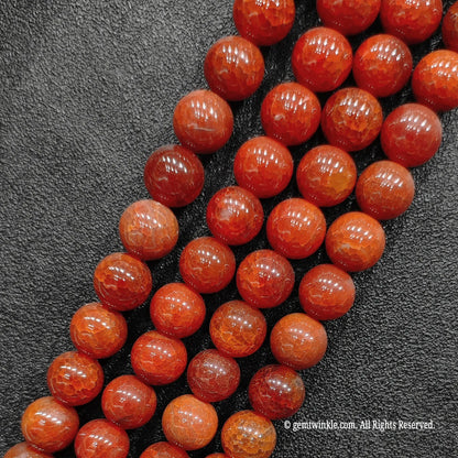 Three bulk strands of fire crackled crimson red agate loose beads aligned on textured dark surface