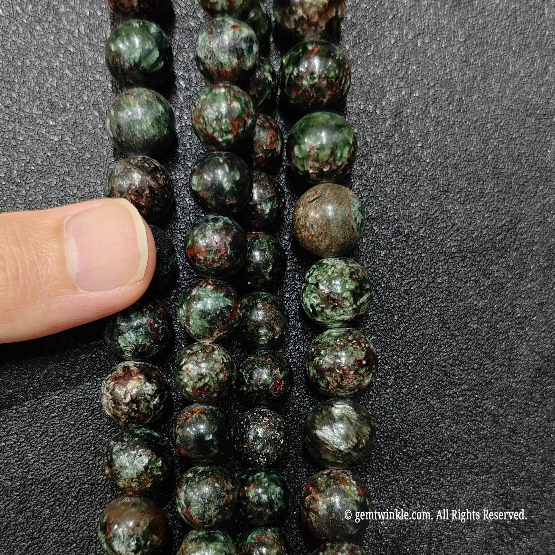 Chunky green crystal bead strands in five to twelve millimeter sizes being held for inventory quality review